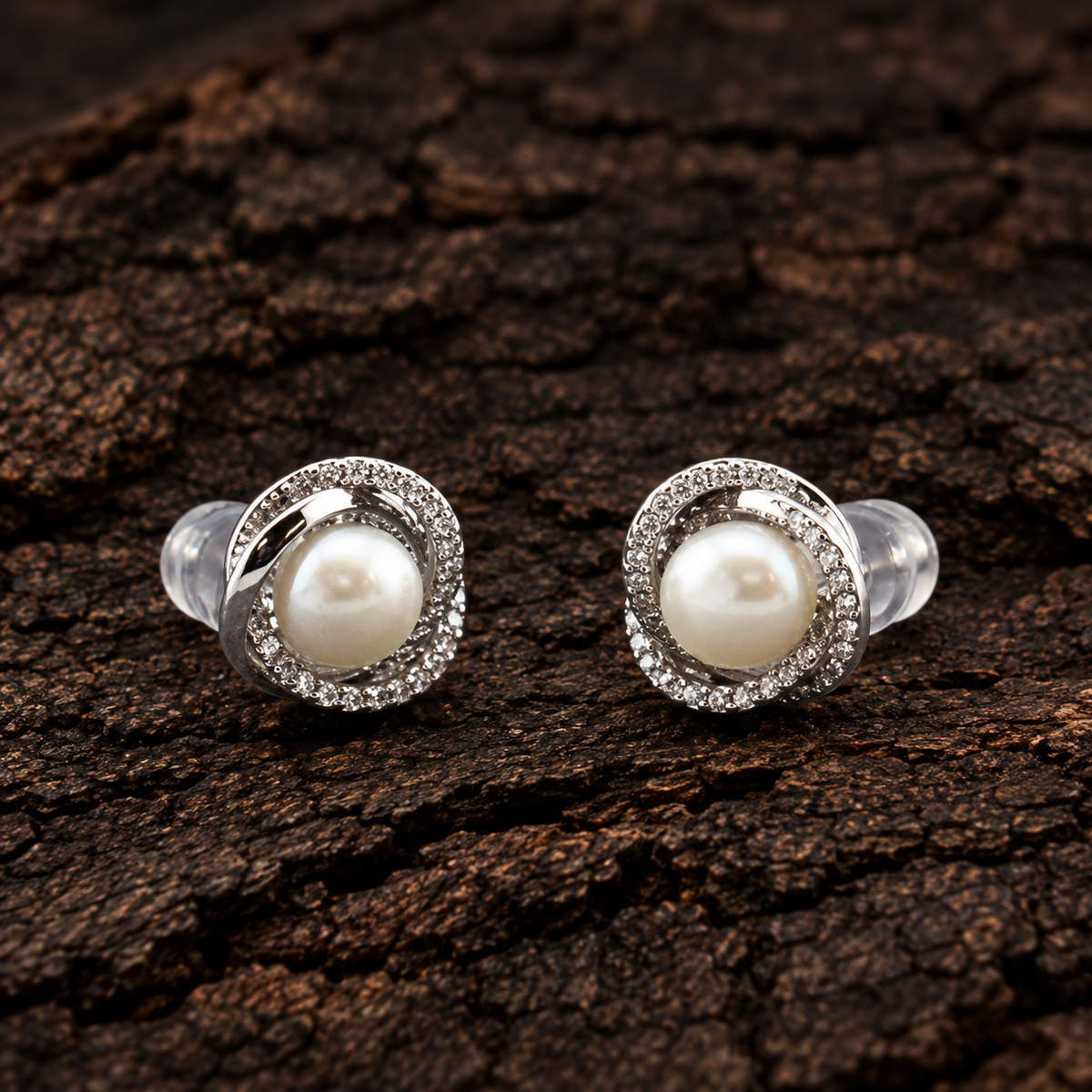 925 sterling silver pearl stud earrings with sparkling CZ swirl design on dark wood background.