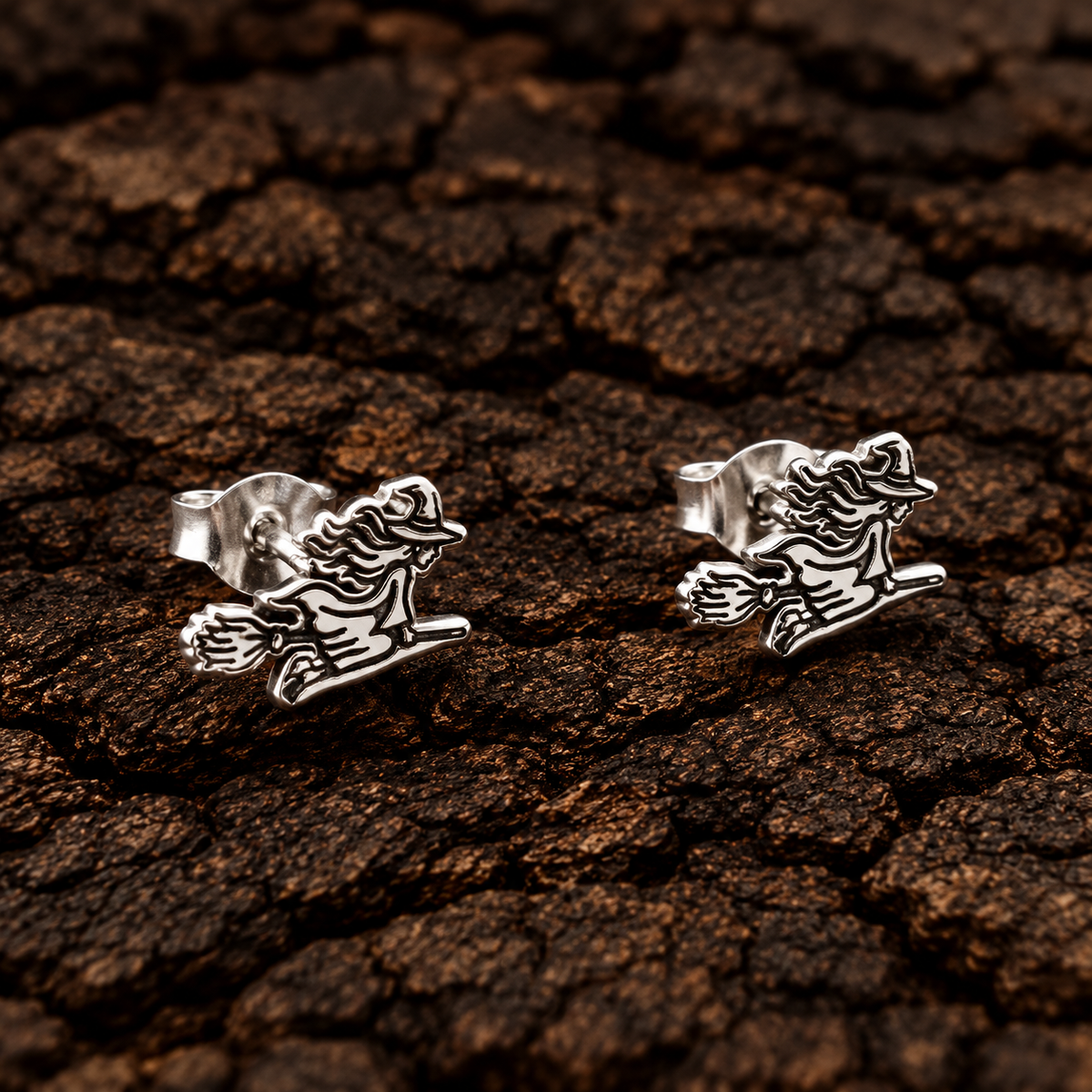 Sterling silver witch on broom earrings with detailed black accents on bark background