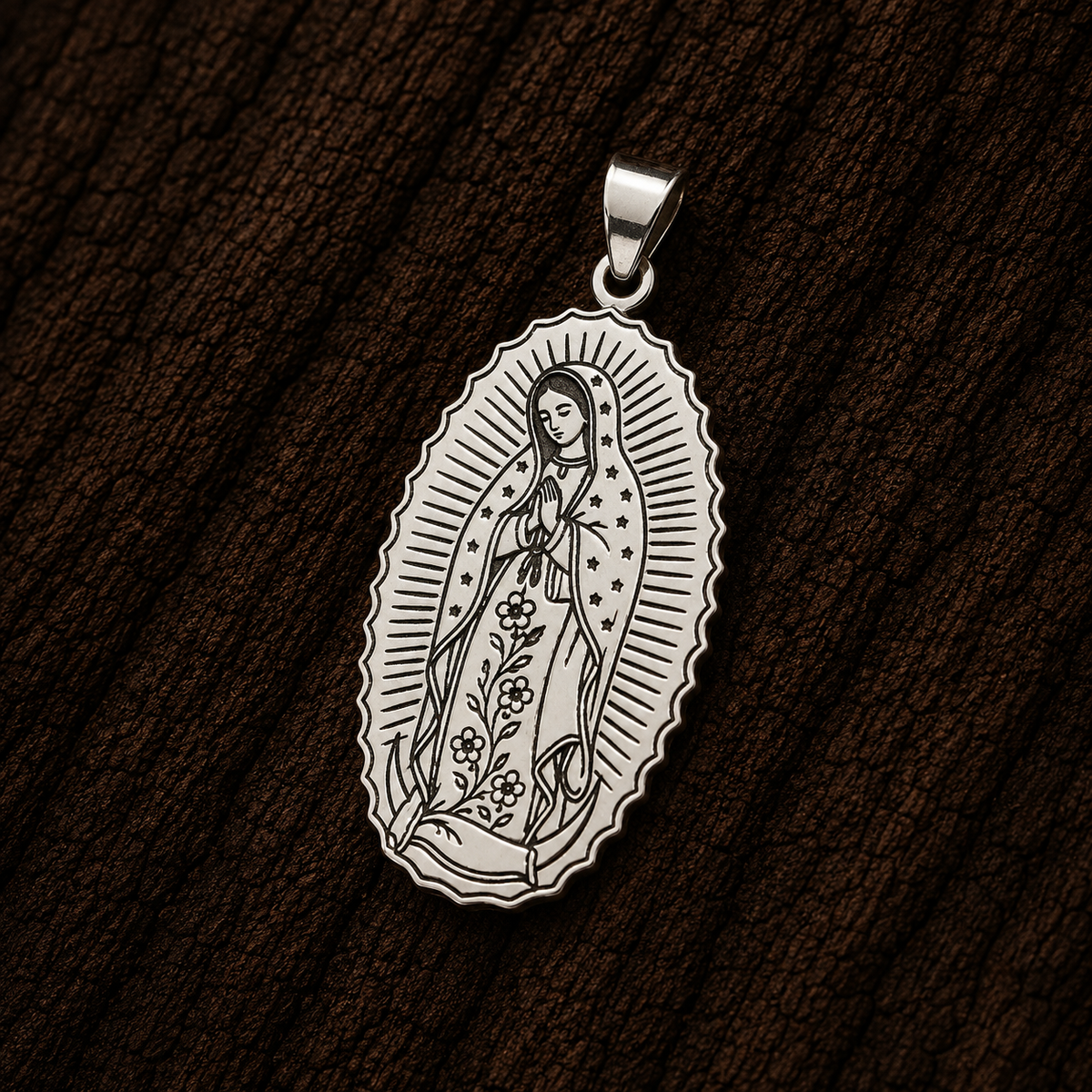 Our Lady of Guadalupe silver pendant with detailed floral engraving, displayed close-up against a dark wood background.