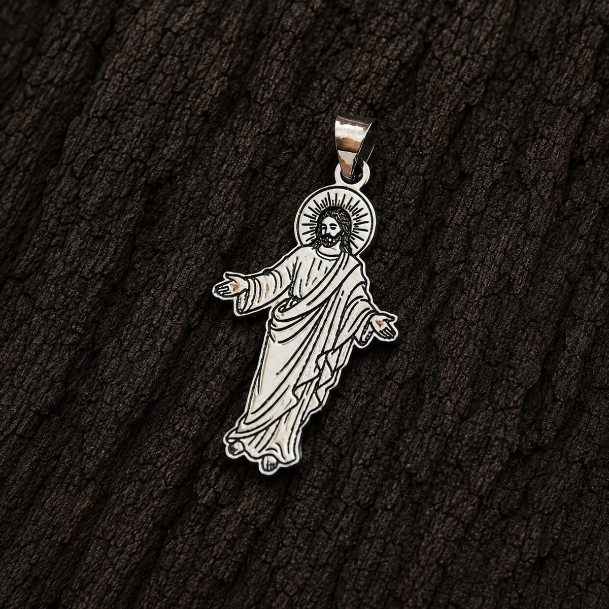 Jesus Christ open arms sterling silver pendant displayed close-up against a dark wood background.
